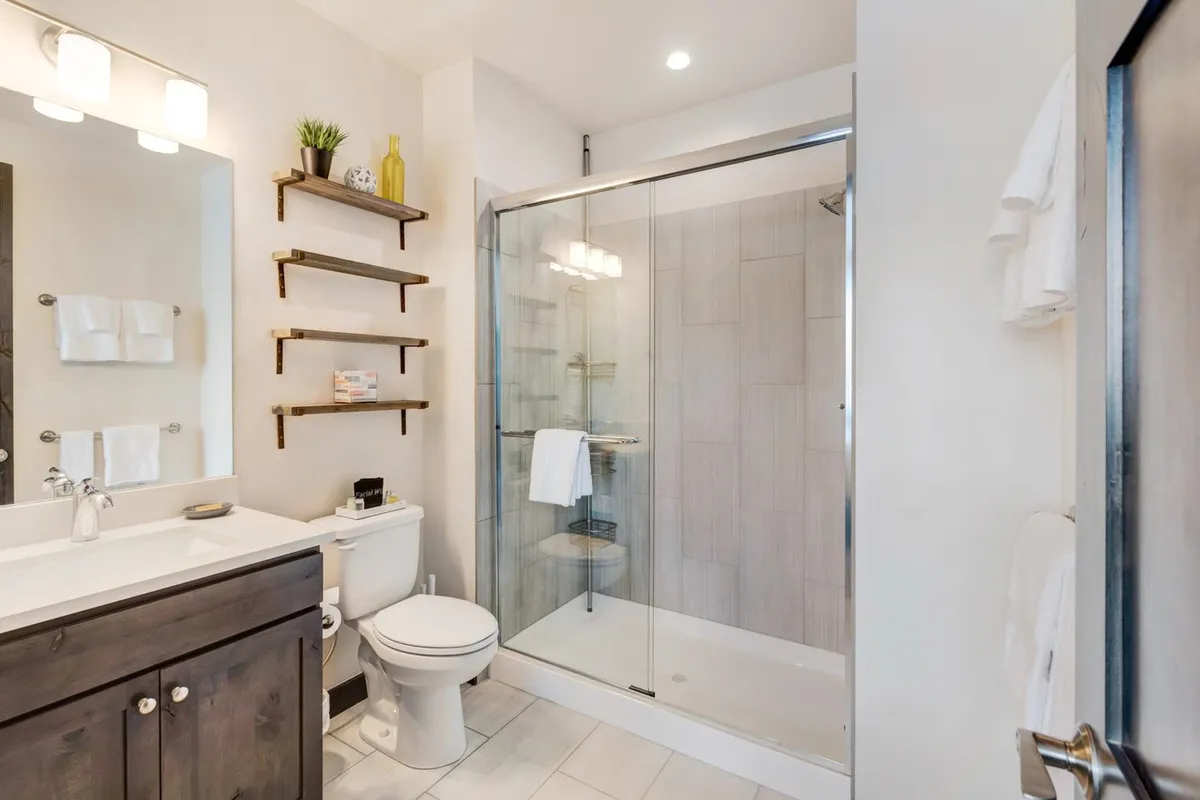A modern bathroom with a glass shower enclosure, sleek vanity, and floating shelves for storage. The ambiance is serene and spa-like, ideal for self-care and refreshing routines.