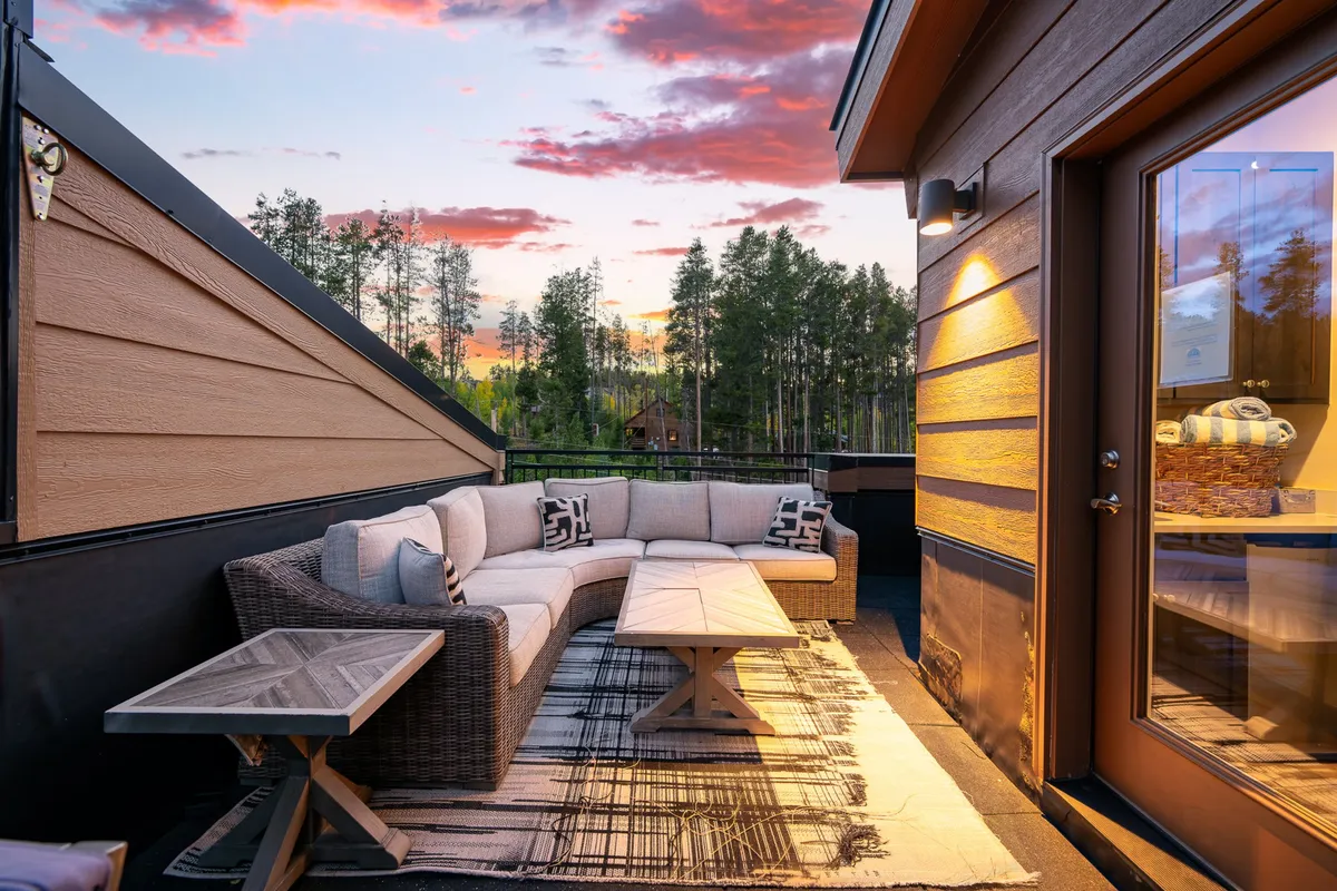 An inviting rooftop outdoor sectional sofa and coffee table, positioned under a stunning sunset sky. The setting suggests a tranquil spot for relaxing, stargazing, or unwinding after a day of outdoor activities, all with sweeping mountain views.