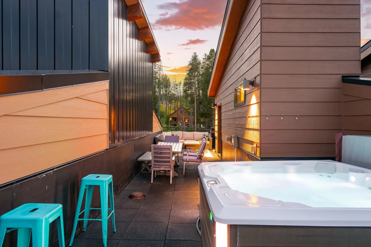 The image features a deck equipped with a hot tub, outdoor seating, a wooden table, and stools—perfect for outdoor dining and socializing. The presence of grilling and relaxation amenities nods to the section’s mention of two gas grills, deck dining, and enjoying the mountain air. The ambient lighting and sunset views add to the mood of relaxed gatherings.
