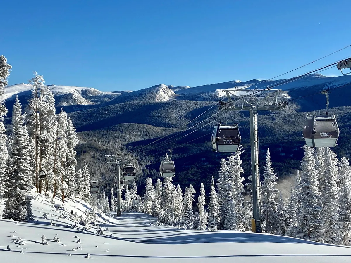 An awe-inspiring exterior shot of ski lift gondolas ascending above snow-covered trees, with rugged mountain peaks looming in the distance. The landscape exudes the thrill and beauty of a winter adventure destination, inviting exploration and excitement.