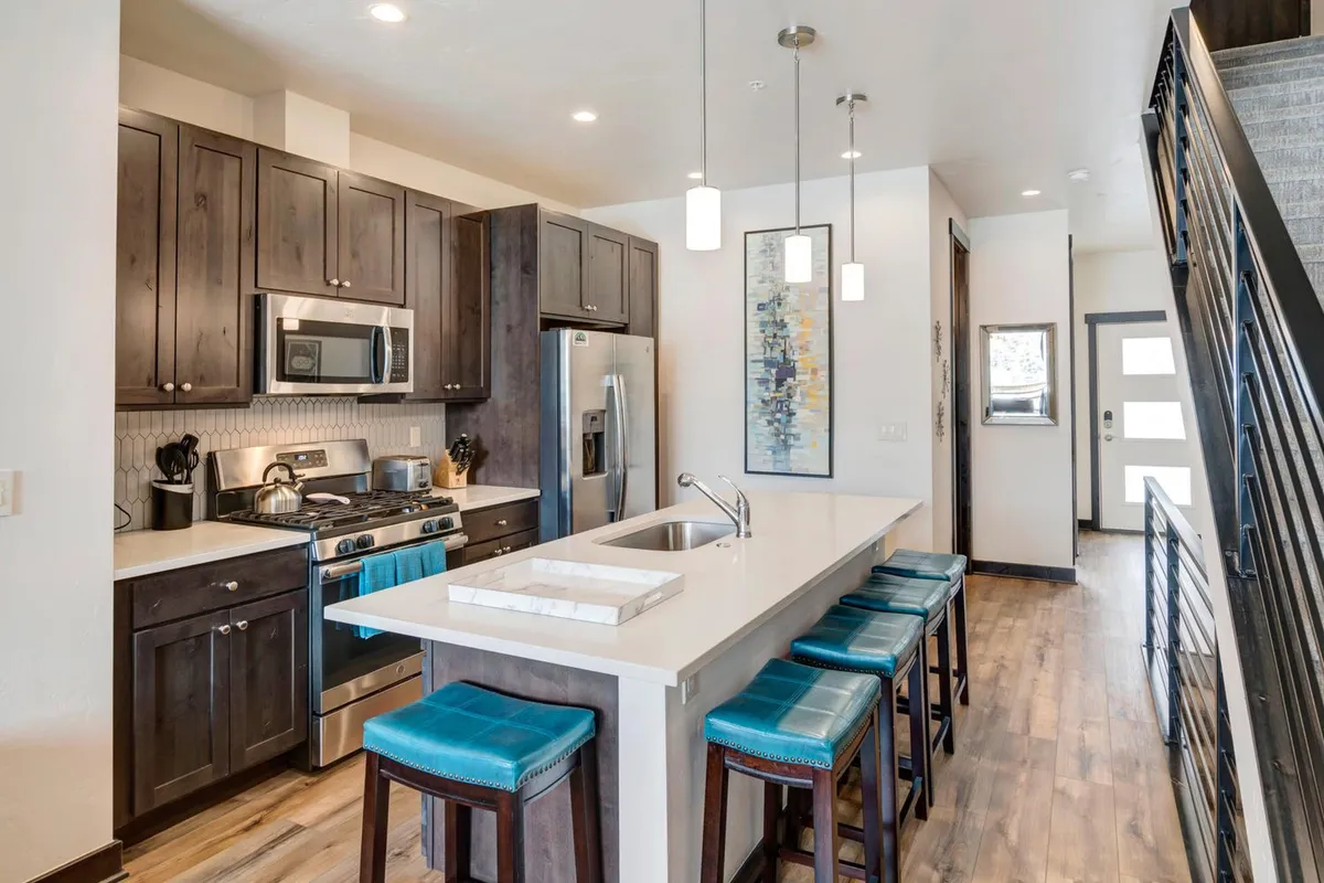 A contemporary kitchen and dining area with a spacious island, sleek stainless steel appliances, and bar stools for casual seating. Walls are adorned with art, and the setup encourages both family cooking sessions and group gatherings over coffee or meals.