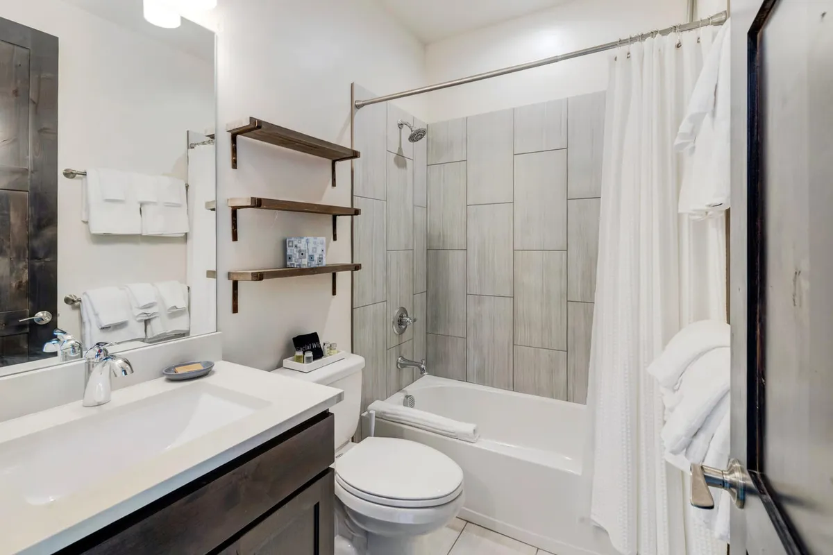 A serene bathroom with a vanity and sink, spacious bathtub, and thoughtfully decorated shelves. The space is bright, inviting, and ideal for relaxation after a day outdoors.