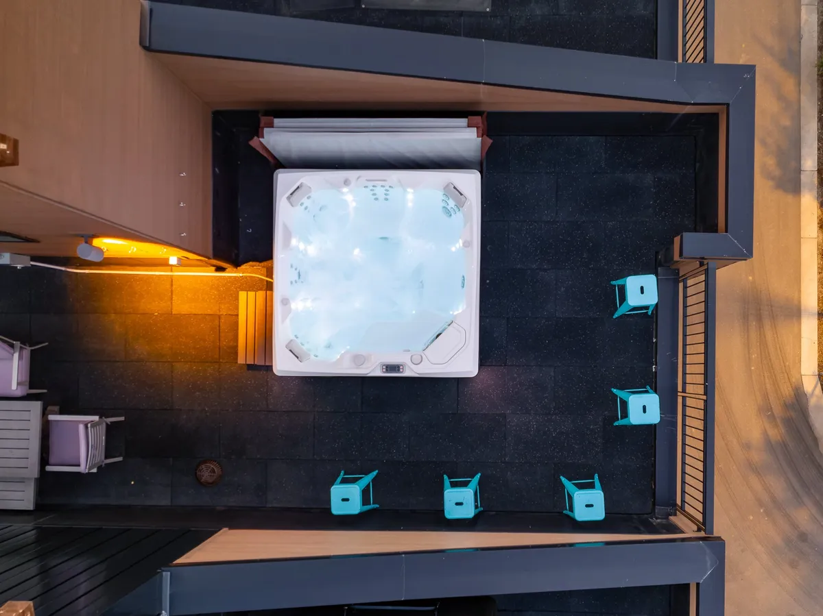 An exterior nighttime view of a hot tub surrounded by comfortable chairs and glowing ambient lights, all set beneath an open sky. The setup is intimate, perfect for soaking, stargazing, and sharing stories with friends.