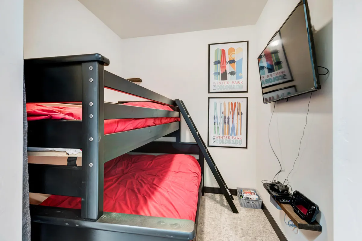 A playful bunk room featuring a bunk bed with vibrant red bedding, a wall-mounted TV, and ski-themed artwork. The setup is ideal for kids or friends, offering a fun and inviting sleeping space.