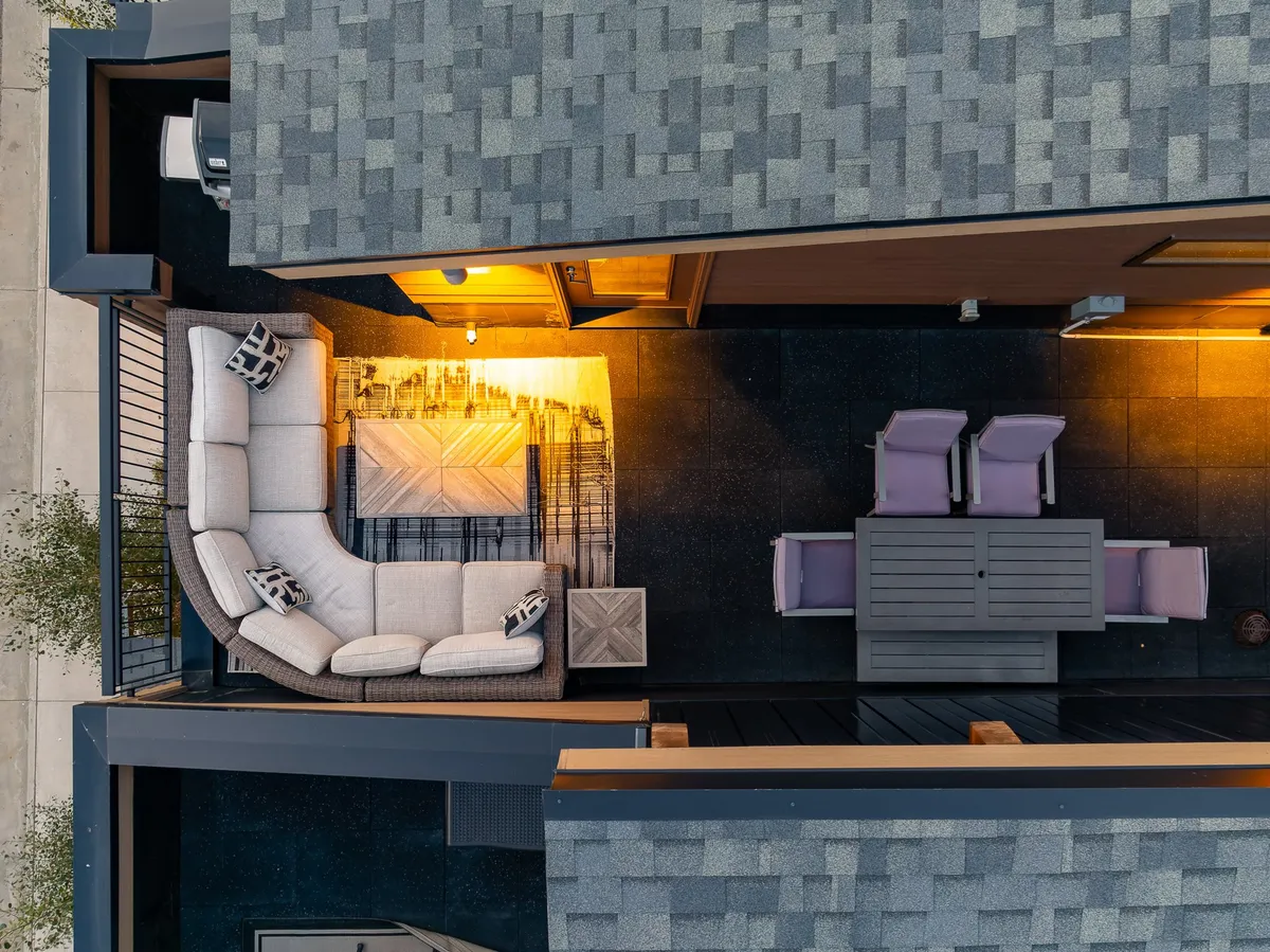 A cozy rooftop patio at dusk, spotlighting a curved sectional sofa and an outdoor dining table with ambient lighting. The scene suggests an inviting space for starlit conversations and group gatherings, with a backdrop of open sky.